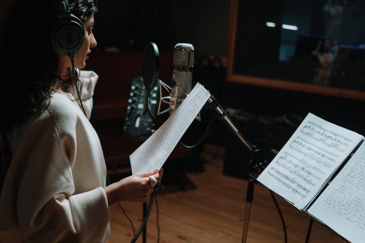 About Woman in a music studio recording a song with a condenser microphone and headphones.