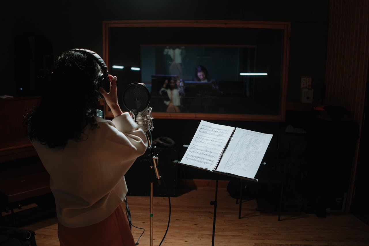 About A female singer records vocals in a professional music studio with a microphone and sheet music.